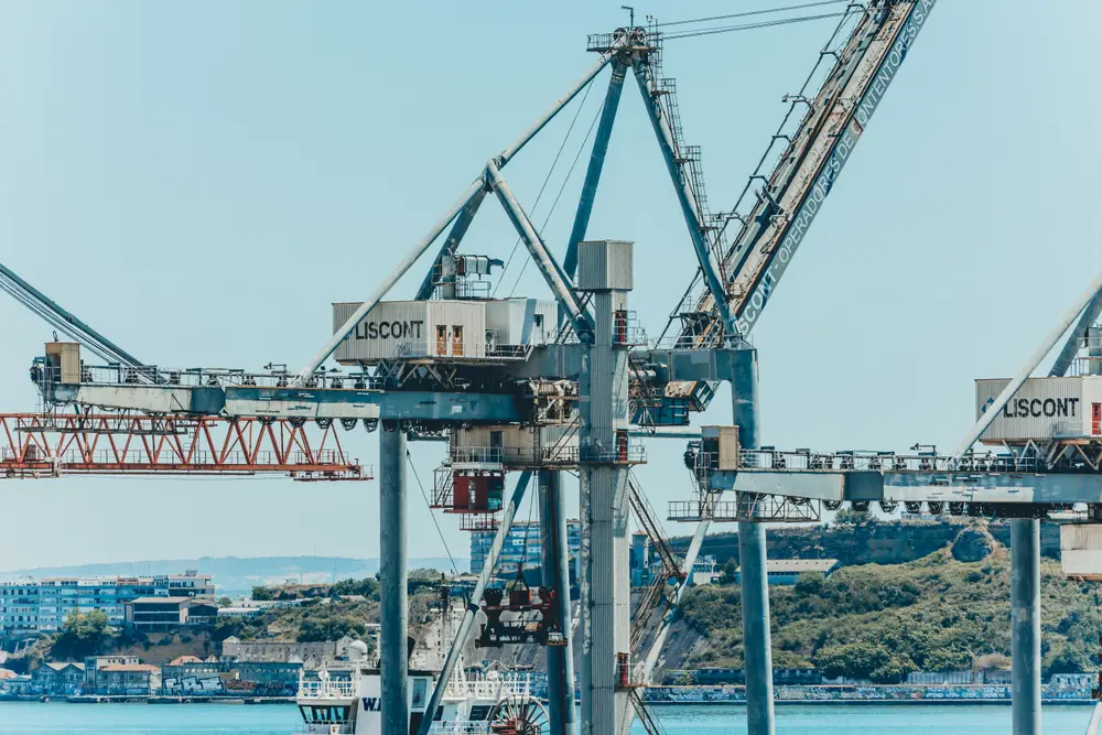 Conjunto de gruas do porto recortadas sobre o rio e a outra margem