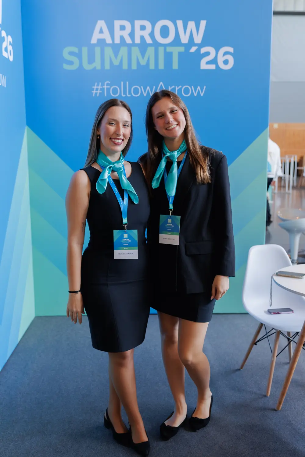 Duas promotoras junto ao painel de boas-vindas do summit