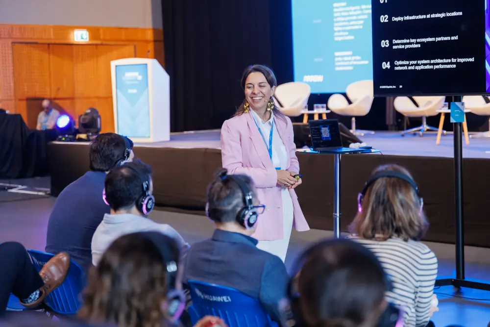 Oradora a apresentar em palco, com a plateia em primeiro plano