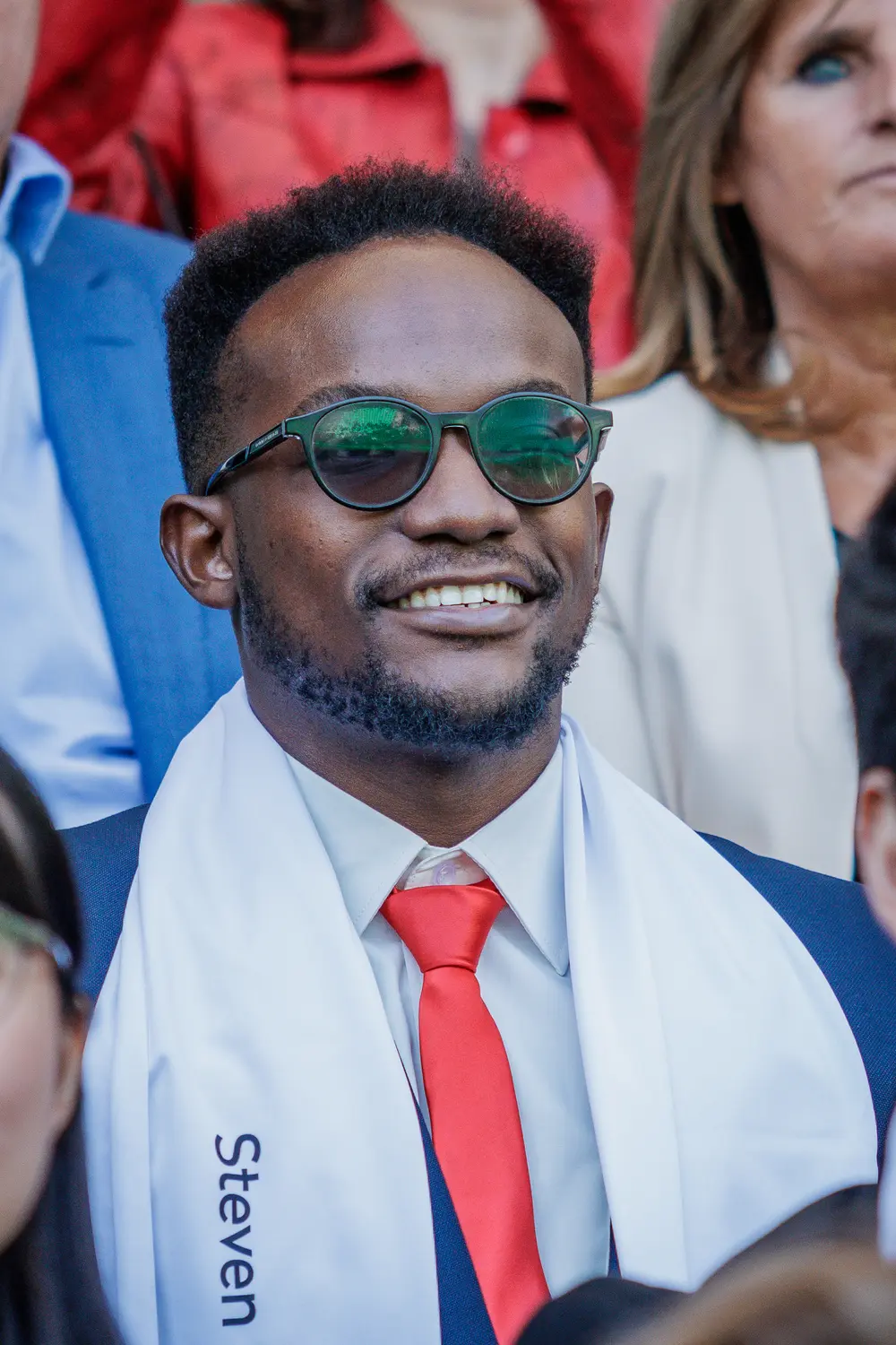 Graduado a sorrir, com óculos de sol e o cachecol da academia