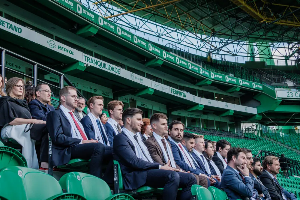 Graduados sentados na bancada, com a arquitetura do estádio atrás