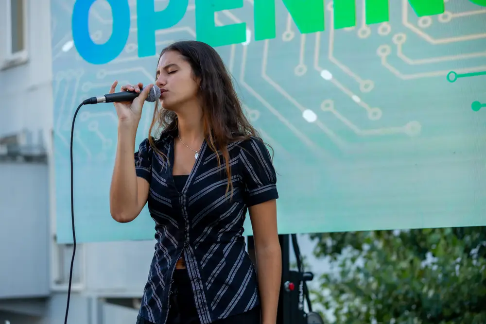 Cantora ao microfone, diante do ecrã da inauguração