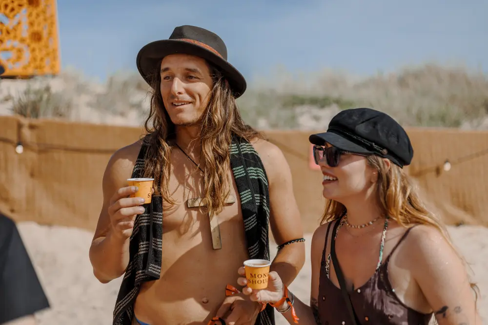 Dois festivaleiros a conversar com bebida na mão, sobre a duna