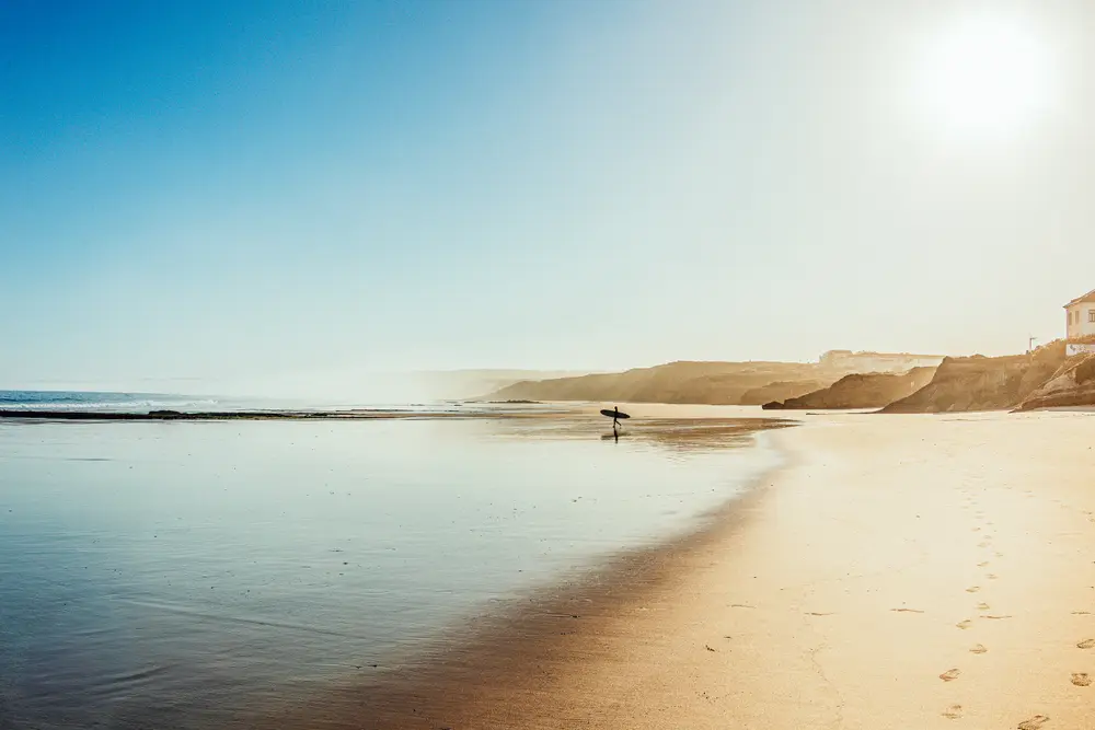 Surfista ao amanhecer, entre a praia e o mar