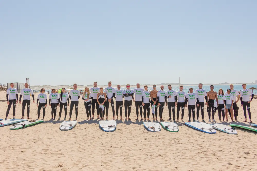 Fotografia de grupo da equipa na praia, com as pranchas
